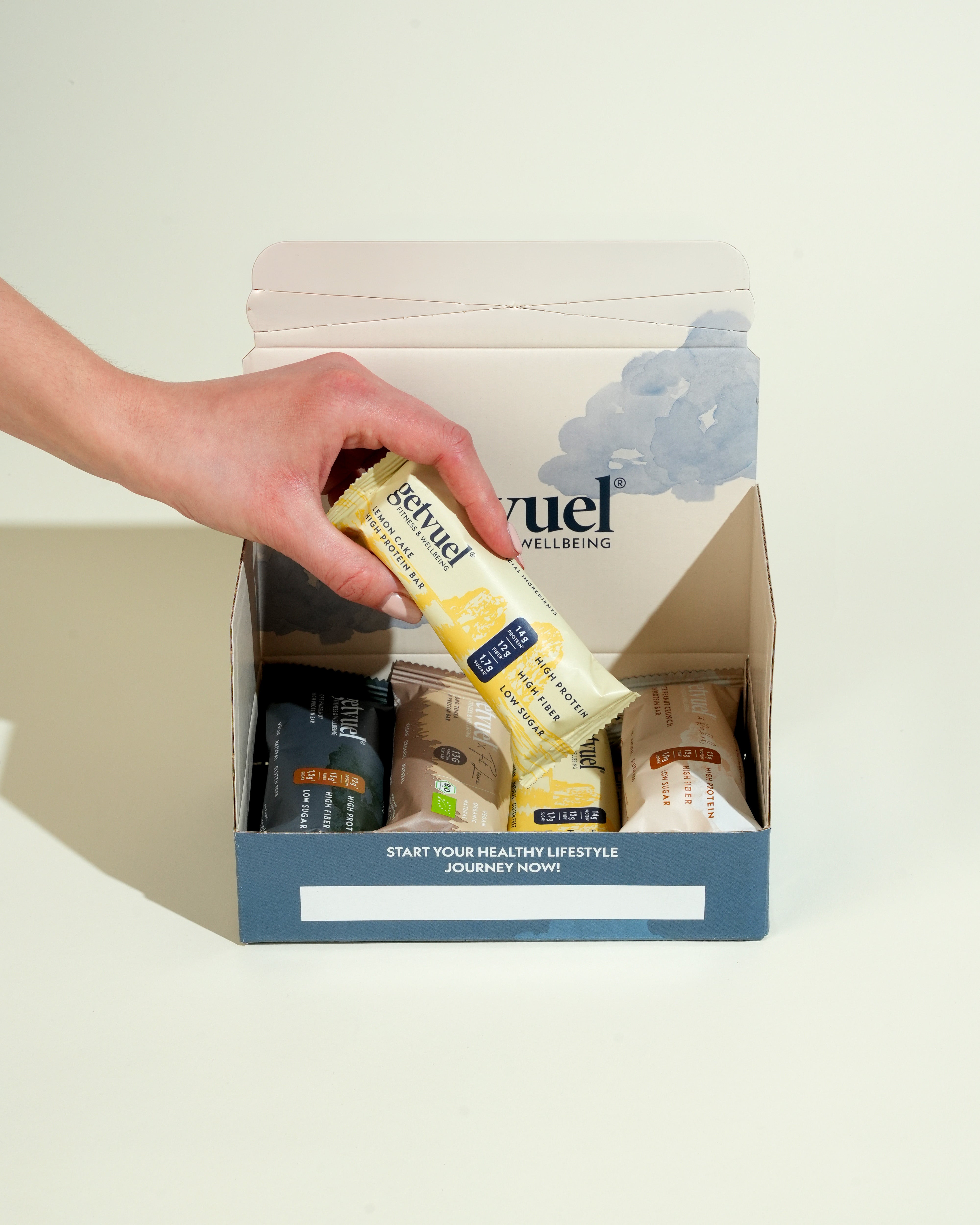 Proteinriegel von getvuel – Probierbox mit vier Sorten – Pack- und Detailansicht mit Hand